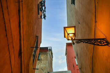 Sticker - Low-angle view of the pastel colored medieval houses in a narrow alley of the historic centre of Sanremo at dusk, Imperia, Liguria, Italy