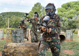 Wall Mural - Paintball players aiming and shooting with a marker guns at an opposing team outdoors