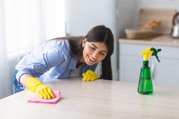 Wall Mural - Cheerful young woman cleaning dining table at kitchen