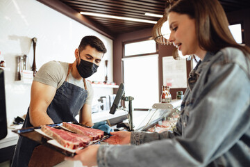 Butcher's shop seller helps to choose product to woman customer