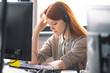 Beautiful young Caucasian red hair girl with hands on head dressing casual with headache or migraine working in the office or class at the desk in front of two monitors. Stress and overwork concept