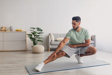 Wall Mural - Fit millennial Arab guy stretching his leg, working out at home during covid lockdown, copy space