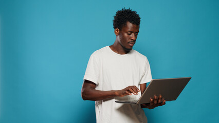 Young person holding laptop with internet connection. Portrait of adult looking at modern device screen in studio over isolated background. Man with gadget and online technology.