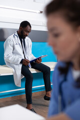 Wall Mural - General practitioner with coat looking at checkup documents, waiting on patient at examination appointment in medical office. Specialist reading papers to treat disease and sickness