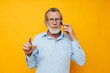 © Tatiana - old man in a blue shirt and glasses talking on the phone yellow background