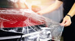 © Parilov - Process of pasting hood of red car with protective vinyl film from gravel chips and scratches. Transparent protection for paint