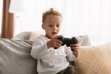 Wall Mural - African Little Boy Playing Videogame Sitting On Sofa At Home