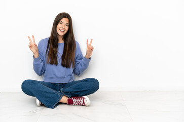 Young woman sitting on the floor showing victory sign with both hands