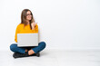 © luismolinero - Young caucasian woman with a laptop sitting on the floor isolated on white background pointing to the side to present a product