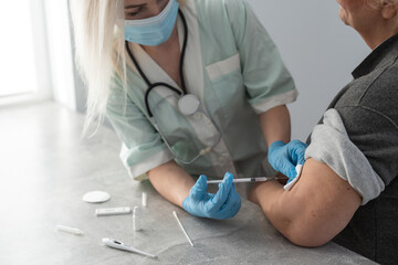 Wall Mural - Physician in medical face mask holding syringe while senior lady keeping arm