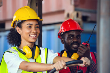 Two African American male and female worker in uniform and helmet driving and operating on diesel container forklift truck at commercial dock site.