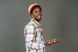© Svyatoslav Lypynskyy - Young black man in afro hat smiling happy gesturing with open hands half lifted up. Cheerful african american young man in plaid shirt looking at camera isolated on gray background