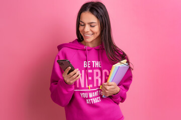 Wall Mural - hispanic pretty woman in pink hoodie smiling holding holding notebooks and using smartphone