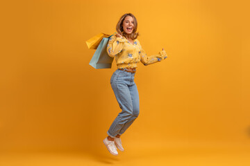Wall Mural - beautiful attractive smiling woman in yellow shirt and jeans with shopping bags