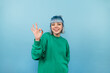 © bodnarphoto - Positive lady in green sweatshirt and colored hair shows gesture ok to camera and smiles, isolated on blue background.