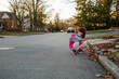 © Cavan Images - Little girl squats down in street to write notes in journal at sunset