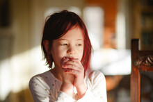 A Shy Little Girl With Dyed Red Hair Sits Alone With Hands Clasped