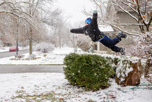 Boy Leaping Athletically In Mid-air Off Snow-covered Rock In Winter