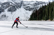 © Cavan Images - Young man playing ice hockey on lake near snow covered mountain