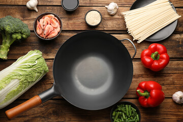 Empty iron wok and raw ingredients on wooden table, flat lay