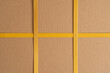 Brown cardboard box tied with yellow strapping tape. There are two crossings of the tape. Background. Texture. Form.