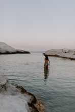 Young Female Traveller Influencer And Blogger Is Enjoying The Day At Sarakiniko Beach In Milos On A Sunny Summer Day Surrounded By White Cliffs And Rocks, Turquoise Waters Of Aegean Sea At Sunset