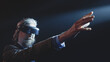 © Framestock - Middle aged male creator showing viewers, how augmented reality glasses work near LED screen and touching something in the air during a Metaverse event in a dark lit room with spotlights
