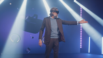 Developer in a casual suit on stage presenting and talking about new virtual reality headset for the Metaverse, conference in a dark lit room opposite the LED screen with 3D objects