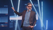 © Framestock - A mature businessman in a suit on stage telling the audience about the financial success of company and investments in front of an LED screen with graphs, during the presentation of business strategy