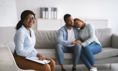 Wall Mural - Smiling black female psychologist and young married couple hugging after successful marital therapy at office