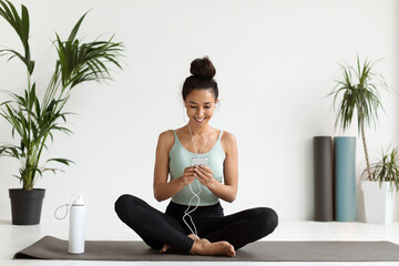 Wall Mural - Smiling Woman Relaxing With Smartphone On Yoga Mat Before Training In Studio