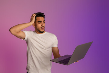 Wall Mural - Shocked young Arab man with laptop computer touching his head in panic, missing work project deadline in neon light