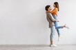 © Prostock-studio - Side view of romantic young Asian guy holding and hugging his beloved girlfriend against white studio wall, copy space