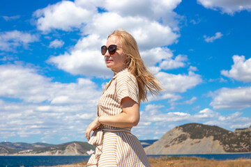 Young blonde woman on the background of the sea and mountains on a summer sunny day. Travel and tourism