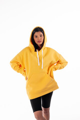 Wall Mural - Attractive woman of Latin appearance wears a yellow hoodie on a white background. The girl looks sexy and happy. The elegant brunette is wearing a bright sweatshirt. All-season clothing