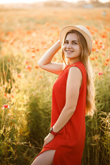 Happy cheerful woman walking on blooming field poppies. Red flowers. A blonde in a red short dress and a hat.