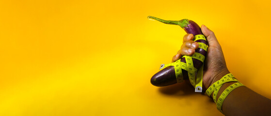 Close-up view of Purple eggplant on hand with copy space wrapped with yellow measuring tape isolated on a yellow background. Concept of healthy eating, dieting, increasing penis size in men, viagra