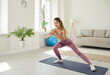 © Studio Romantic - Happy beautiful slim young woman having fitness workout at home. Active young Caucasian girl in modern sports leggings doing side lunge exercise standing on gym mat in living room