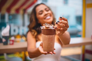 Close-up portrait of happy attractive smiling woman holding a chocolate milkshake with focus on milkshake