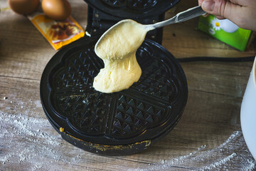 Sticker - A photo of a person putting waffle batter in a waffle iron pan