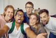 © Studio Romantic - Happy students taking funny selfie indoors.Group of joyful young multiethnic friends having fun together, taking selfie on mobile phone, making hilarious grimaces, sticking tongues out, squinting eyes