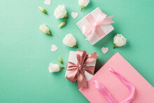 Top View Photo Of Two Small White Gift Boxes With Cute Silk Bows White Eustomas And Small Confetti In Shape Of Hearts Near The Big Pink Gift Bag On The Pastel Turquoise Background