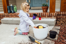 Little Girl In Rain Boots Digging In Pot Of Dirt In Spring