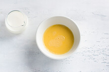 A White Bowl With Beaten Egg And Jug Of Milk On Light Blue Background, Top View. Cooking Omelet, Homemade Healthy Food