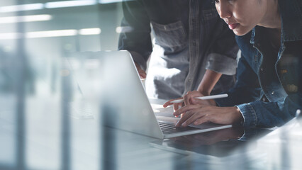 Close up of two asian colleagues working together, have a discussion and using laptop computer at office with financial document on desk