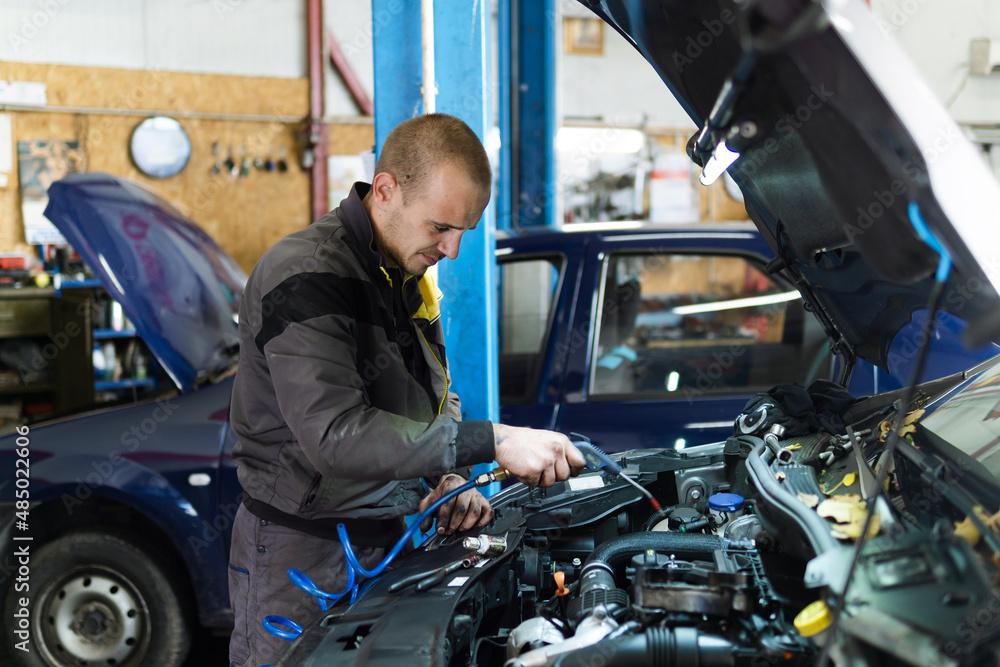 Handsome mechanic in uniform is working in auto service garage. Repair service.