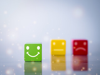 Customer satisfaction survey concept. Close up happy smiley face, blurred neutral and sad face icon on wood cube to survey feedback, rating, review, service satisfaction.
