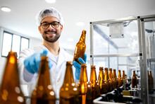 Portrait Of Professional Experienced Technologist Worker Standing In Beer Bottling Factory Checking Product Quality. In Background Production Line Machine And Beer Bottles In Line.