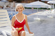 © luengo_ua - UV protection and suntan. Senior woman holding bottle with sunscreen lotion near swimming pool.