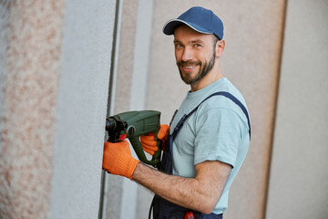 Wall Mural - Cheerful male builder drilling wall with electric drill